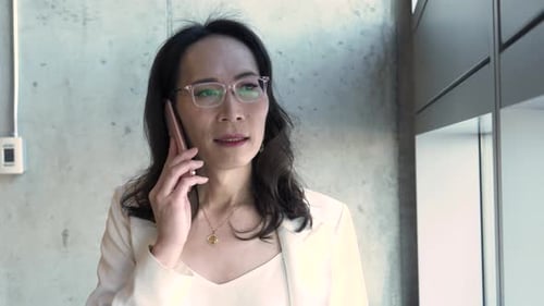 Mature businesswoman in eyeglasses talking on smart phone in office