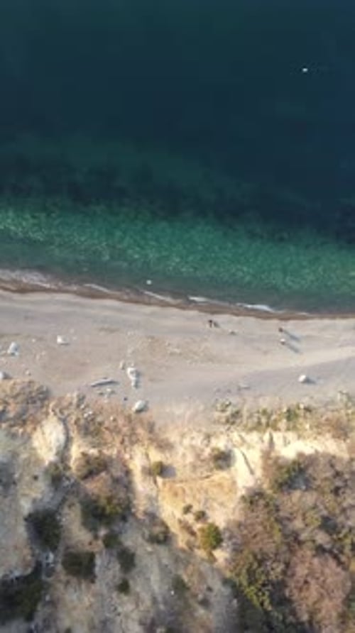 Aerial Vertical View of Beach with Wave Caressing Shore Sun Glare Small Waves on the Water Surface
