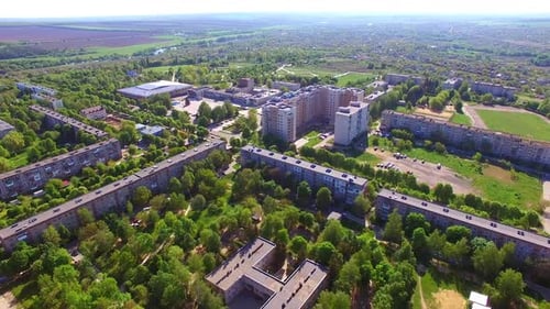 Sunlit panorama of a city with blocks of flats and green streets.