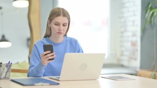 Woman Using Phone and Laptop at Work