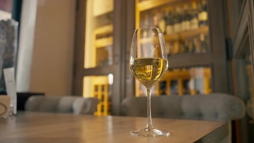 Close-up of a glass of white wine standing on a table in an Italian restaurant against a wine rack
