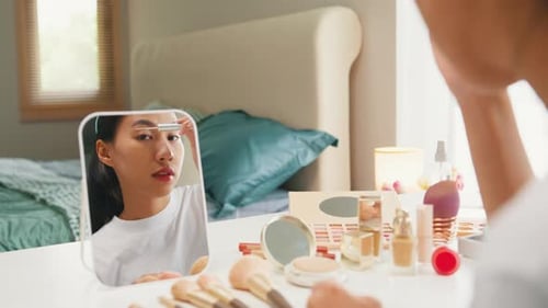 Young happy Asian girl beauty blogger looking at mirror makeup use eye lash mascara top coat serum.