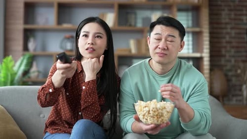 Couple Watching TV, Eating Popcorn on Couch Indoors