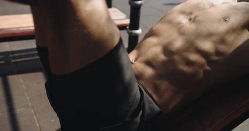 Shirtless Man Doing Leg Raises On Outdoor Bench