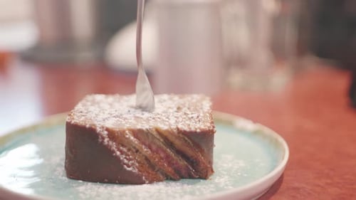 Close up of a piece of cake on a plate topped with powdered sugar and a fork. Shot in 4K