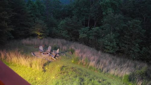 A fire pit outside of a cabin in the woods at night in the summer.