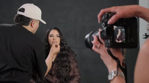 Un fotógrafo filma cómo un maquillador pinta los labios de una modelo de pelo negro
