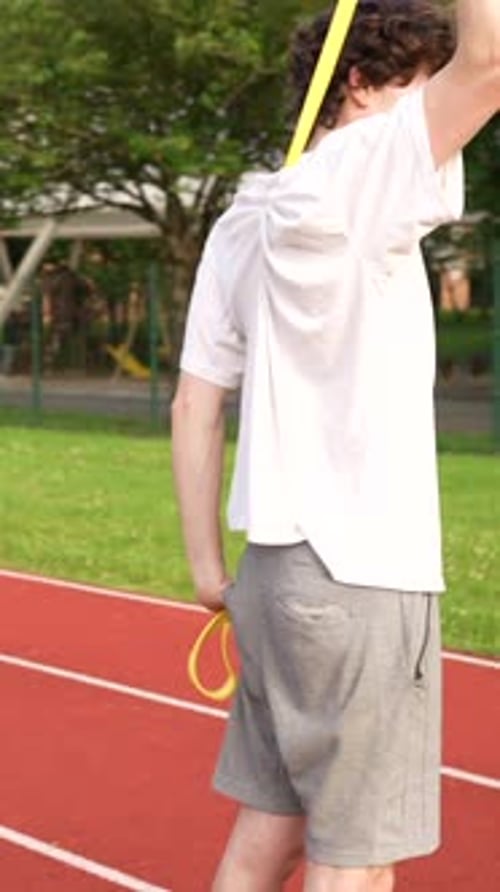 Young Man Stretches on Track with Resistance Band