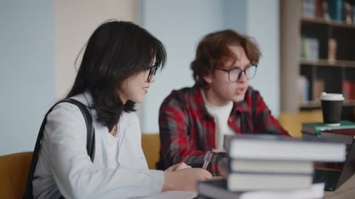 Two university students collaborating on a project in the library