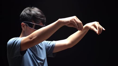 Side View Of Asian Man Carrying And Looking Invisible Objects While Using Futuristic Goggles
