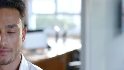 Half portrait of happy biracial businessman smiling at office, with copy space, in slow motion