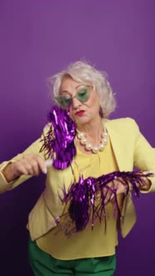 Stylish Senior Woman with Pom Poms on Purple Background