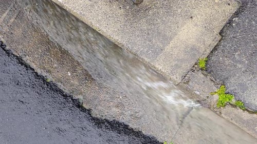 Fast flowing rain water flowing down curb side drainage on road during wet raining weather