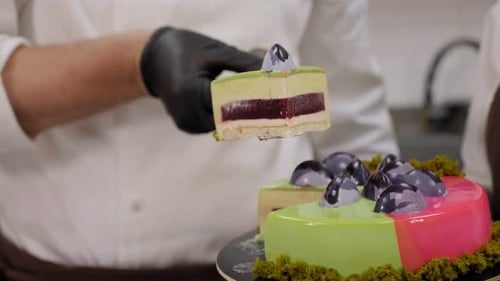 Un primer plano de un chef con guantes cortando un pastel de mousse con un glaseado de espejo verde