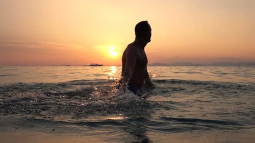 Man splashing water playfully in the tropical sea at sunset super slow motion