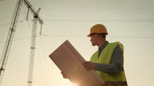 Energy Auditor Consulting Blueprints During Transmission Tower Inspection