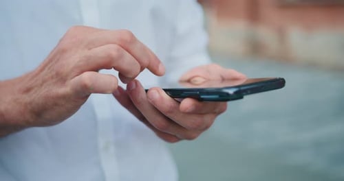Close up male hands holding smartphone walking at street in City. Man texting messages on his modern