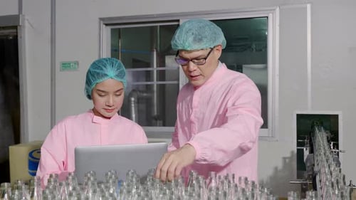 Deux ingénieurs supervisent le contrôle qualité en vérifiant les bouteilles de produits sur le tapis roulant d'une usine de boissons