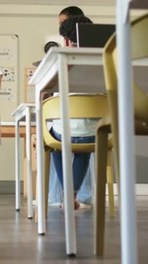 Vertical video: Leaning student moving while laptop showing in classroom, adult leaning in guiding