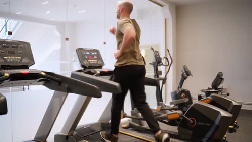 Young Man in Sportswear Running on Treadmill in Front of Window at Gym