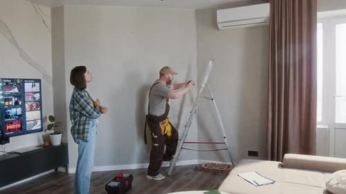 Tradesman Adjusting Air Conditioner Watched by Woman