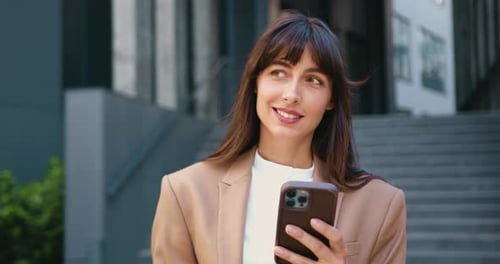 Close-up of happy young professional woman holding smartphone and smiling while looking to the side