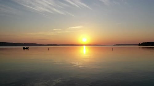 Beautiful skimming drone shot of boaters fishing during golden hour with the sun setting over Lake G