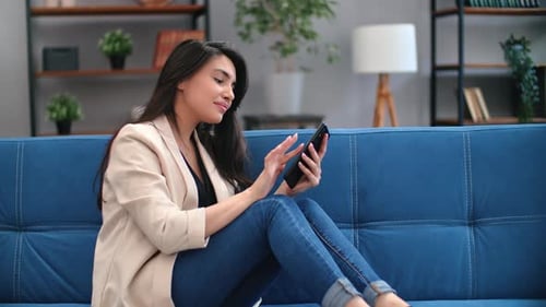 Smiling Woman Using Smartphone on Couch at Home