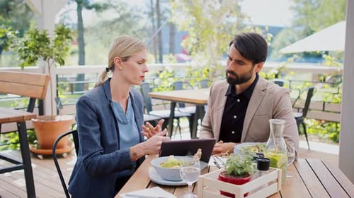 Business partners discussing issues on terrace restaurant table with tablet