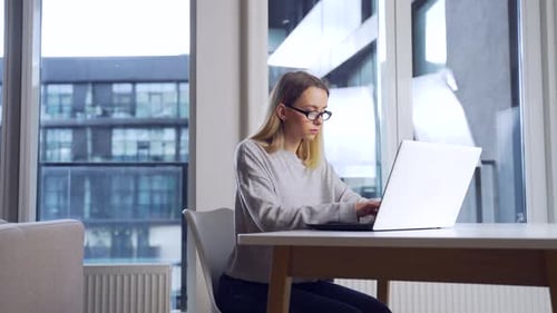 Woman Working on Laptop at Table by Window