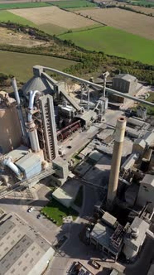 Aerial shot of cement factory infrastructure with pipework, silos, and chimneys in operation near