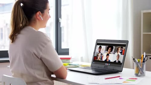 Smiling female teacher in home office leads online video conference with colleagues