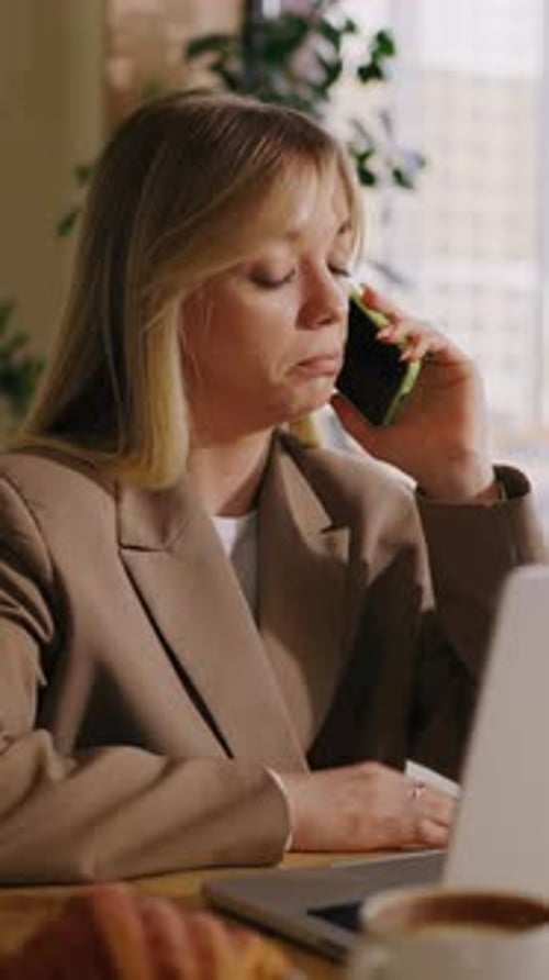 Focused Businesswoman Working at Laptop While Talking on Smartphone During Daytime in Modern Office