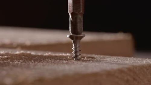 Unscrewing A Screw On A Lumber With An Electric Screwdriver - Woodwork Concept. - macro