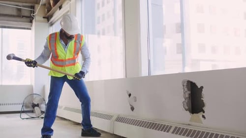 Construction worker knocks hole in vacant office wall in slow motion