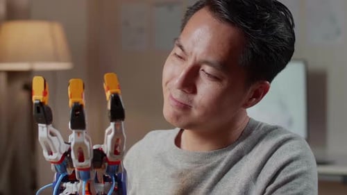 Close Up Of Asian Male Looking And Checking A Cyborg Hand While Working On A Laptop At Home