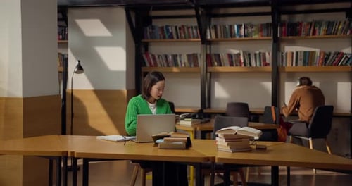 Une étudiante brune est assise à une table devant un ordinateur portable et obtient des informations à partir d'un livre