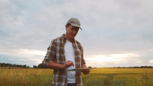 Farmer with a Tablet Computer in Front of a Sunset Agricultural Landscape Man in a Countryside Field