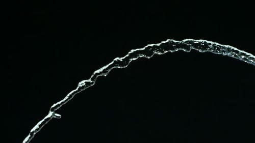 Stream of water arching on black background, abstract