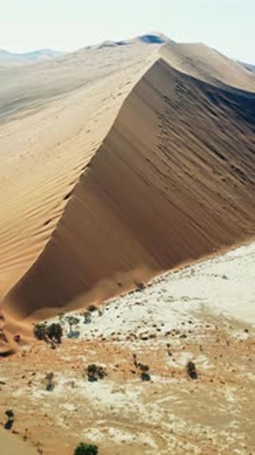 Aerial drone view of a massive triangular sand dune rising above the desert plains in Namibia with s