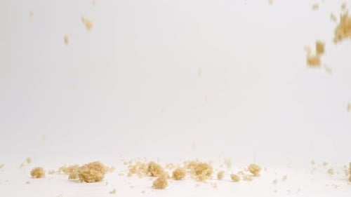 Brown sugar pieces falling onto white studio backdrop in 4k slow motion