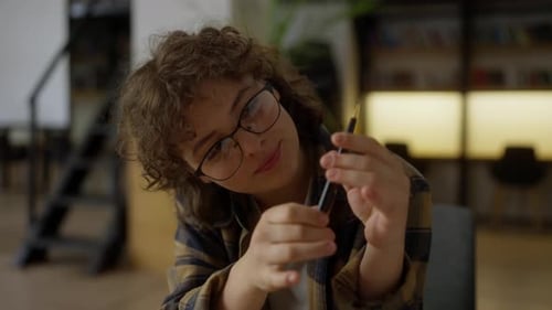Porträt einer glücklichen Studentin mit lockigem Haar und Brille, die ein Buch in der Bibliothek liest
