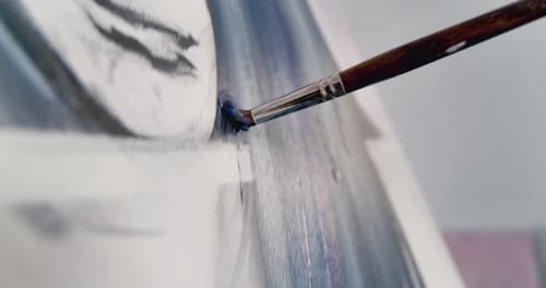 Close-up of the artist's brush painting on canvas, stroking up and down with blue paint. Camera foll