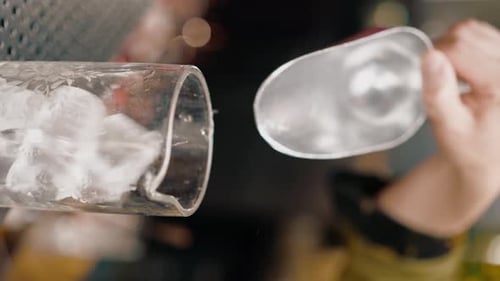 close-up of a bartender pours ice cubes into a cocktail glass in preparation of delicious cocktails