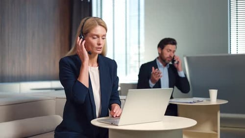 Frau mit Headset hat Videoanruf am Laptop, während Mann auf dem Handy spricht
