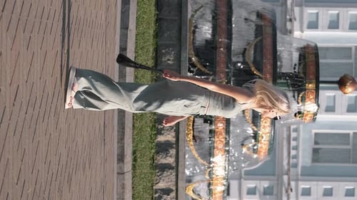 Stylish Woman Walking Near Fountain in Urban Park