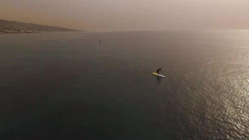 Circle aerial view of man paddling hard on stand up paddleboard on ocean water at sunset