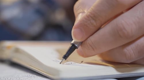 Hand with Pen Writes and Sketches in Notebook