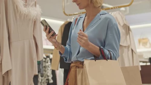 Blonde Woman Texting on Smartphone while Shopping in Boutique