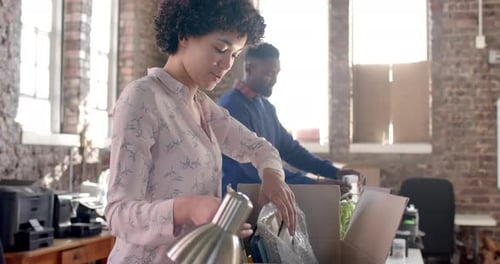 Diverse colleagues unpacking boxes with documents and office items in creative office in slow motion